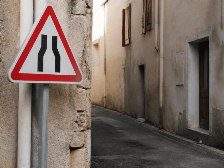 Panneau d'avertissement rouge et blanc pointant vers rue etroite