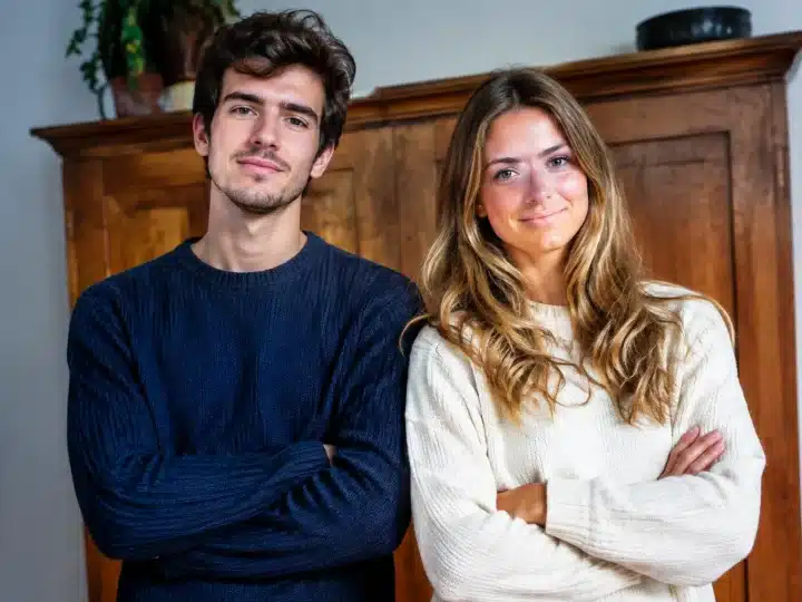 Deux jeunes adultes se tiennent devant un meuble en bois, les bras croisés