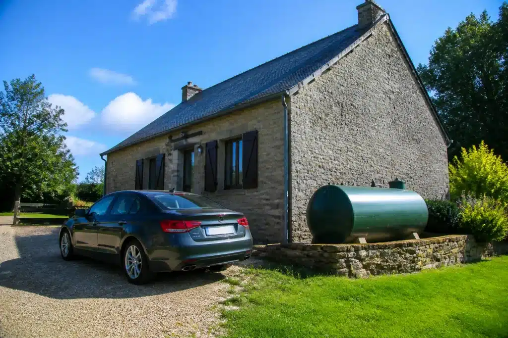 Voiture devant maison rurale avec reservoir fioul visible