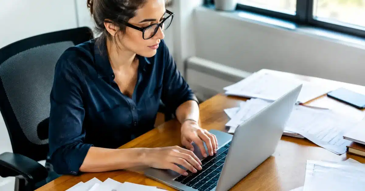 Personne tapant sur clavier d'ordinateur avec documents papier eparpilles a cote