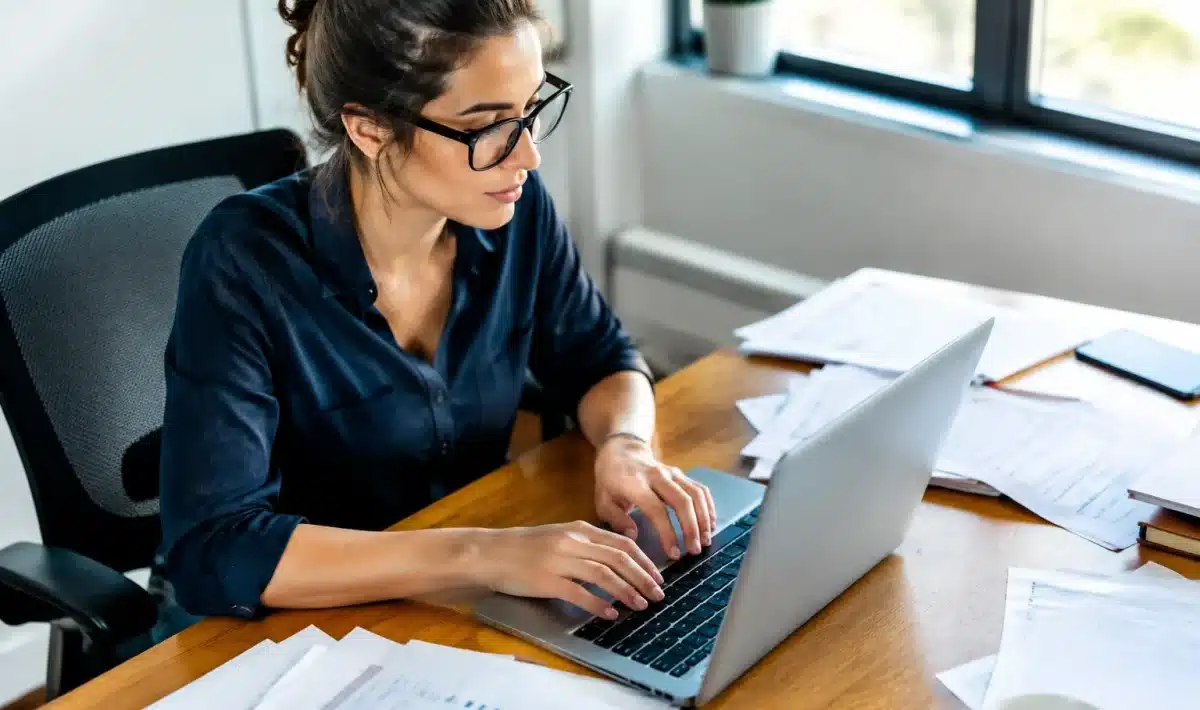 Personne tapant sur clavier d'ordinateur avec documents papier eparpilles a cote