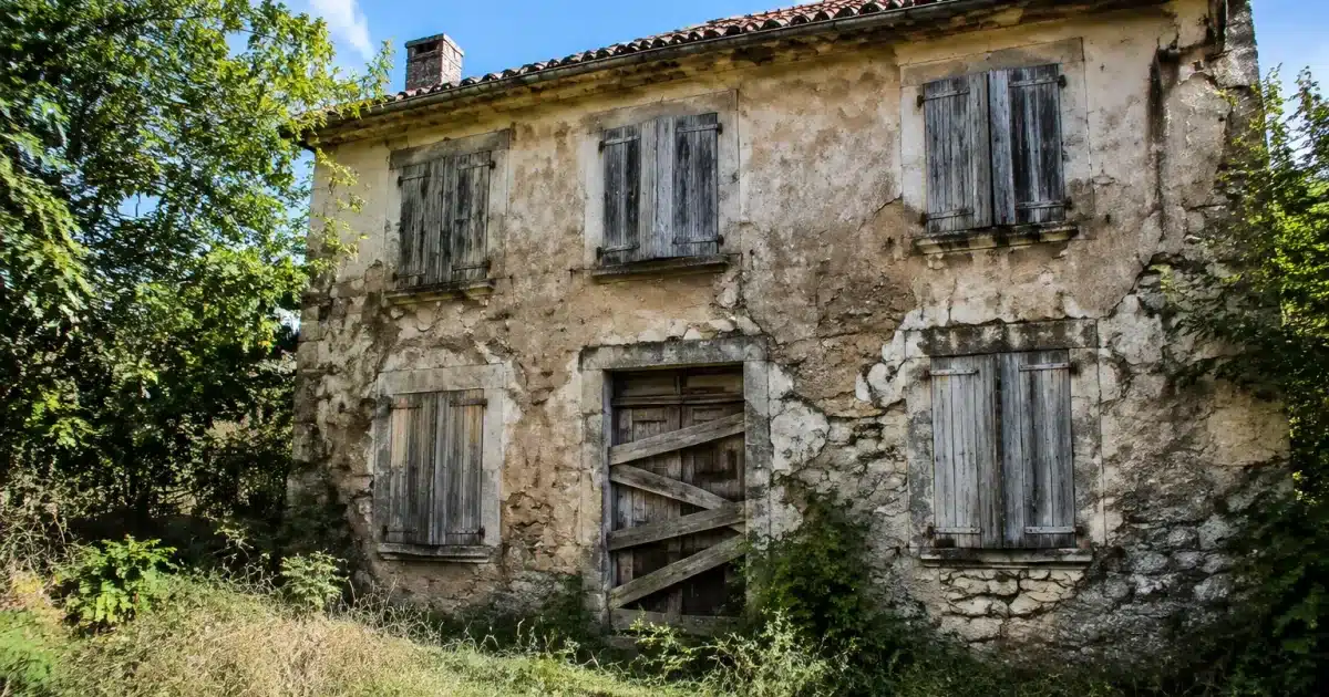 Maison abandonnee aux fenetres fermees, facade deterioree, porte entree barricadee