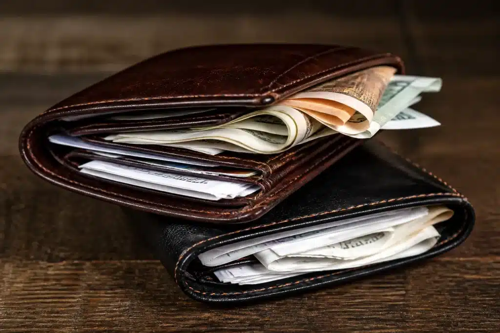 Deux portefeuilles entrelaces avec billets et factures melangees dessus.