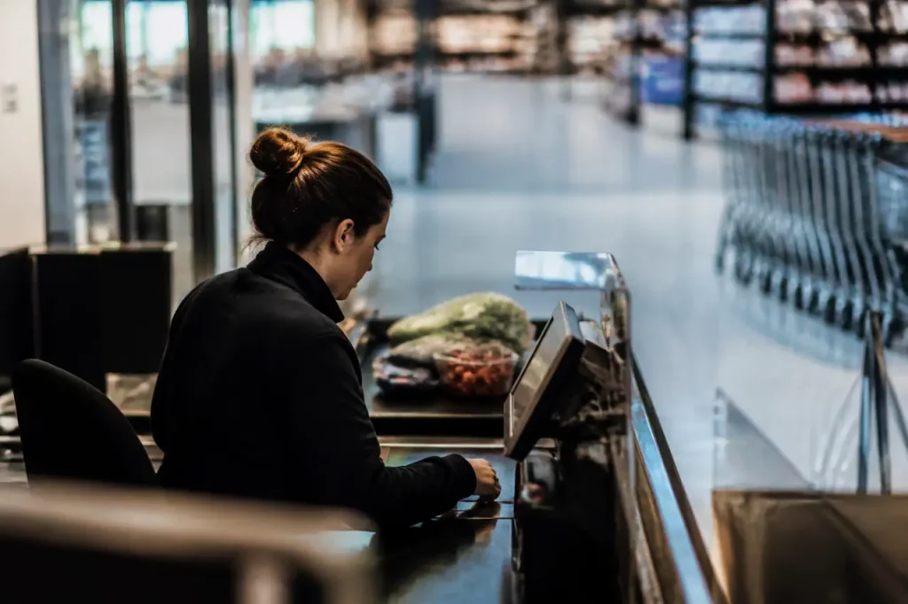 Caissiere devant une caisse, supermarche presque vide, chariots alignes